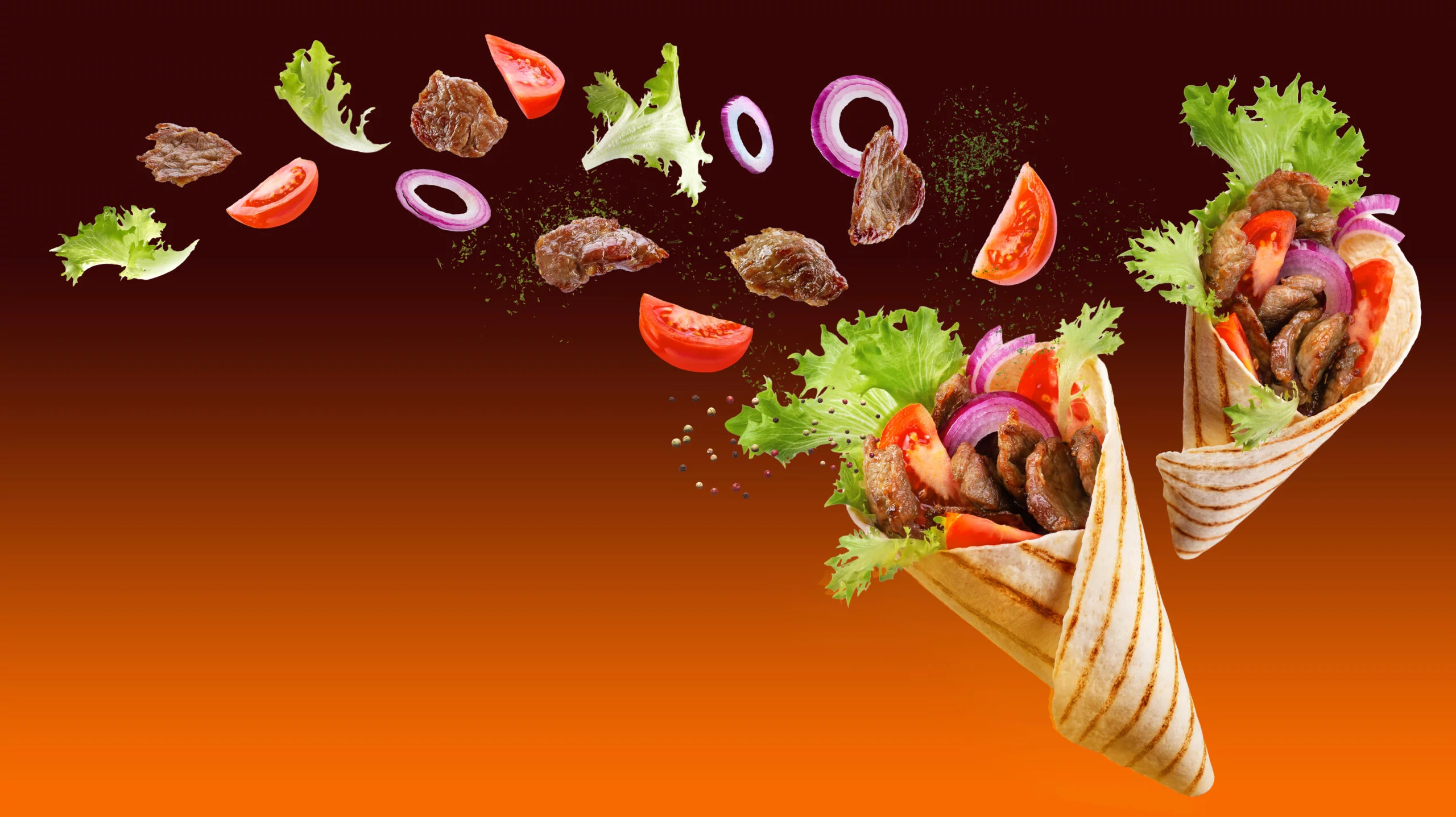 Two doner kebab or shawarma with ingredients floating in the air: beef meat, lettuce, onion, tomatos, spice. Orange brown background. Copy space.